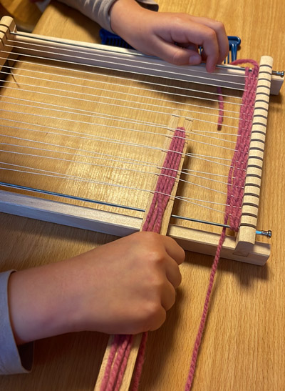 Kind webt mit Webrahmen und Wolle